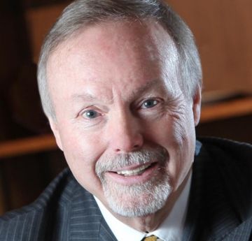 Dyn mewn crys a tei yn gwenu wrth y camera