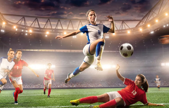 Pêl-droedwraig yn neidio dros chwaraewr arall mewn cit coch mewn stadiwm