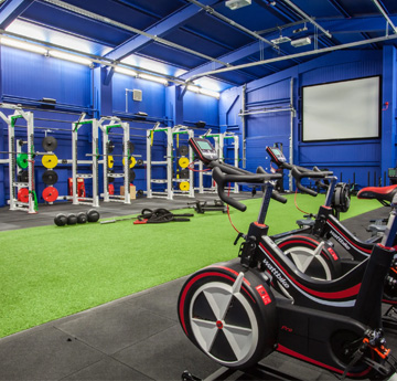 Rheseli pwysau a beiciau campfa mewn ystafell aneglur gyda lloriau artiffisial gwyrdd