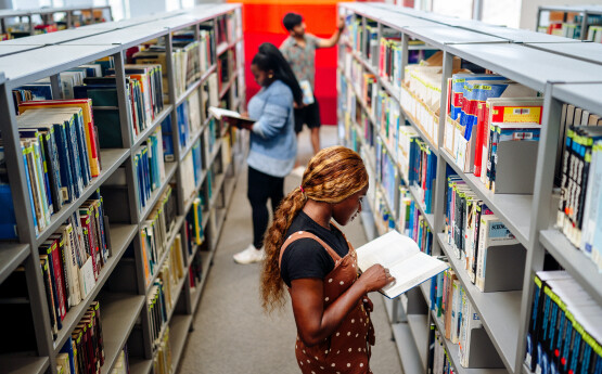 Myfyrwyr yn chwilio am lyfrau ar silffoedd y llyfrgell