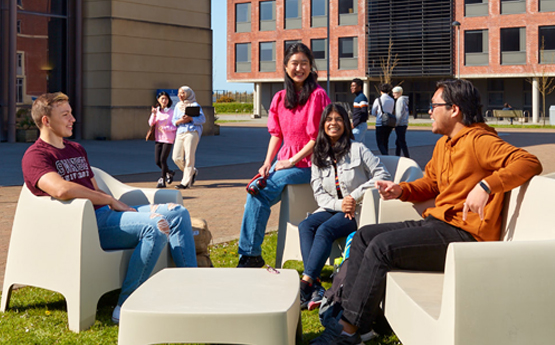 Myfyrwyr yn eistedd y tu allan yn sgwrsio ar Gampws y Bae