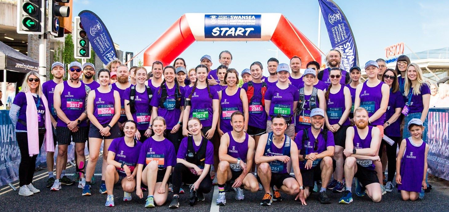 Grŵp mawr o redwyr yn sefyll o dan linell gychwyn y ras