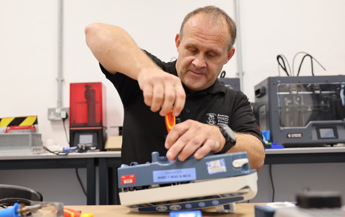 Dyn yn defnyddio sgriwdreifer i atgyweirio peiriant