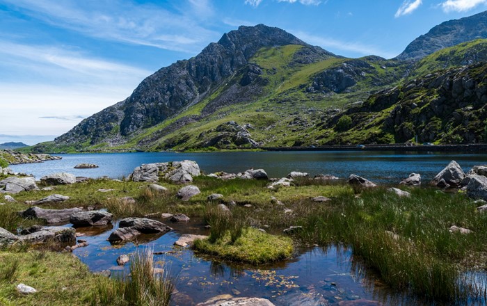 Ardal o ddŵr mewndirol gyda chreigiau a mynydd yn y cefndir yn erbyn awyr las