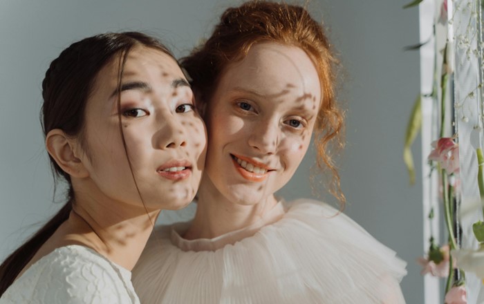 Dwy fenyw ifanc - un Asiaidd, un Cawcasaidd - yn sefyll boch wrth foch yn edrych ar y camera.