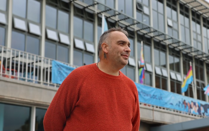 Mark yn sefyll y tu allan i Dŷ Fulton,Prifysgol Abertawe.