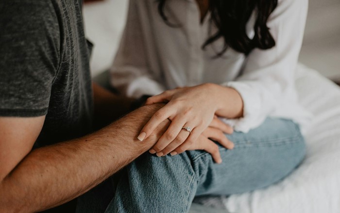 Dyn a menyw yn dal dwylo. Mae'r fenyw'n gwisgo modrwy dyweddio. 