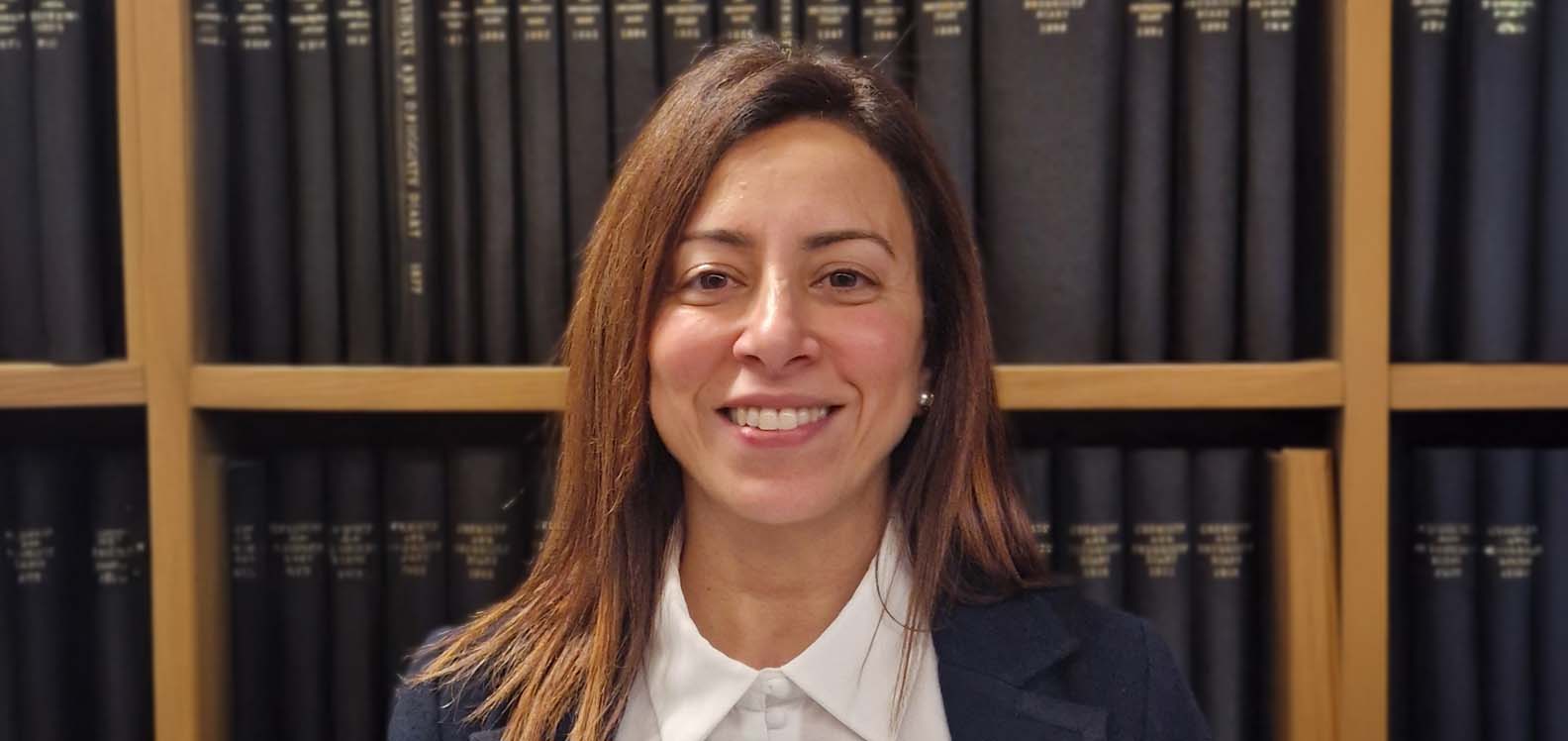 Pen ac ysgwyddau menyw o flaen silff lyfrau