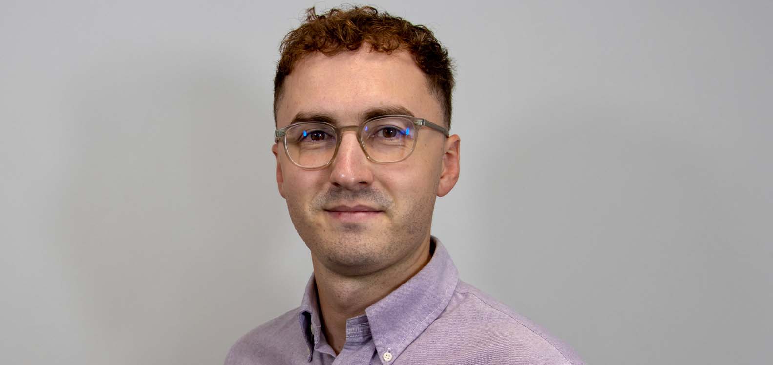 Dyn yn gwisgo crys yn sefyll o flaen cefndir plaen