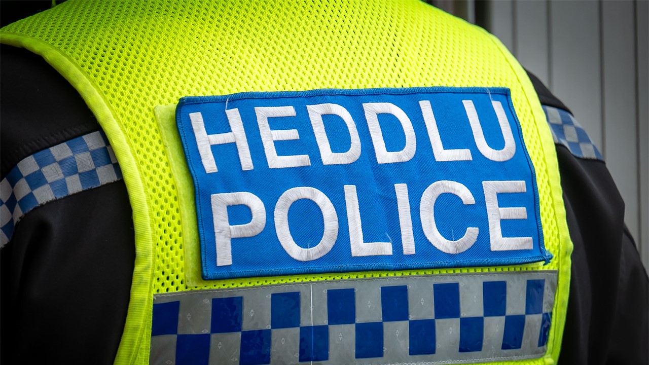 Bathodyn heddlu dwyieithog ar gefn siaced gwelededd uchel