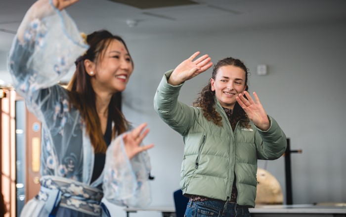 Merch ifanc yn copïo symudiadau dawns a ddangoswyd gan fenyw mewn gwisg Tsieineaidd draddodiadol