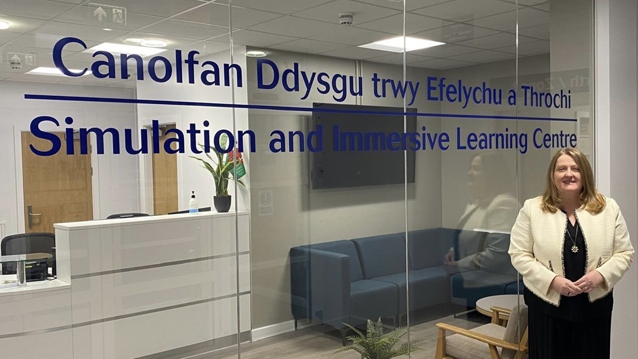 Menyw yn sefyll dan do o flaen rhaniad gwydr