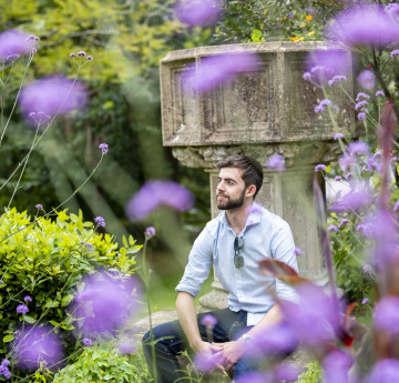 A male student sitting in the grounds of Singleton Abbey - purple flowers are in bloom
