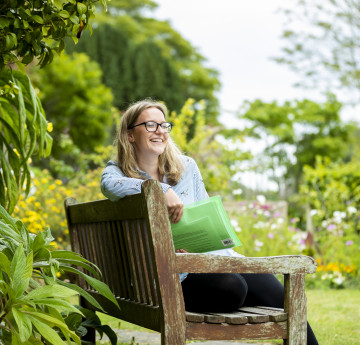 A female wearing a light blue top sits on a bench in the grounds of Singleton Abbey.
