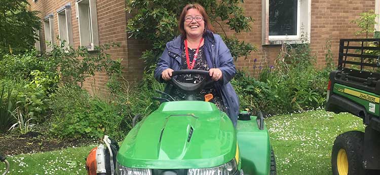 A female staff member learning to drive a grounds lawnmower during a volunteer day