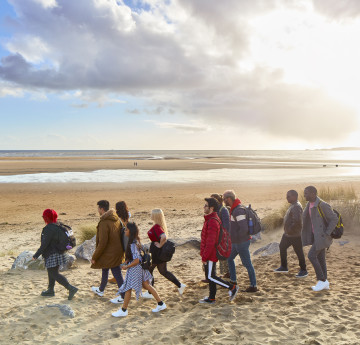 A group of students head down through the dunes to the beach at Crymlyn Burrows