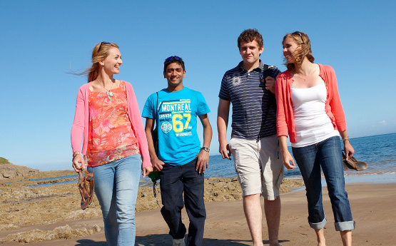 Students walking on the Swansea beach in the sun.
