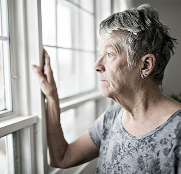 Elderly woman looking out of window. 