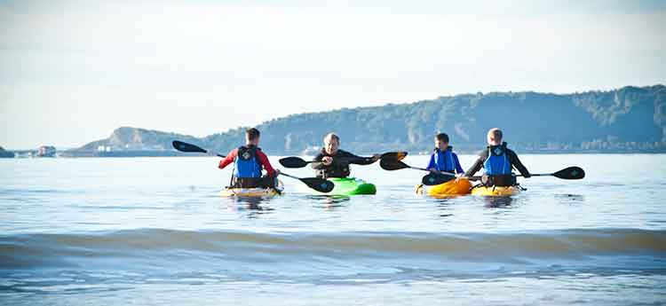 A kayak instructor demonstrates to a group in the water how to use the paddle. 