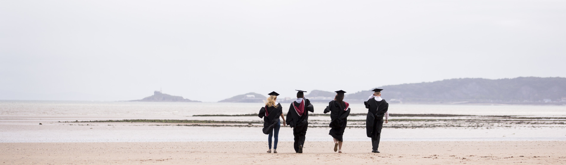Recent graduates in robes walking away on the beach 
