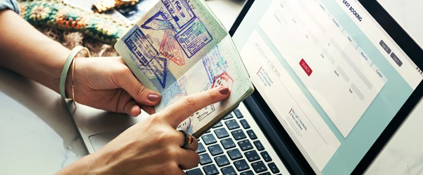 Person pointing at a passport with a computer in the background