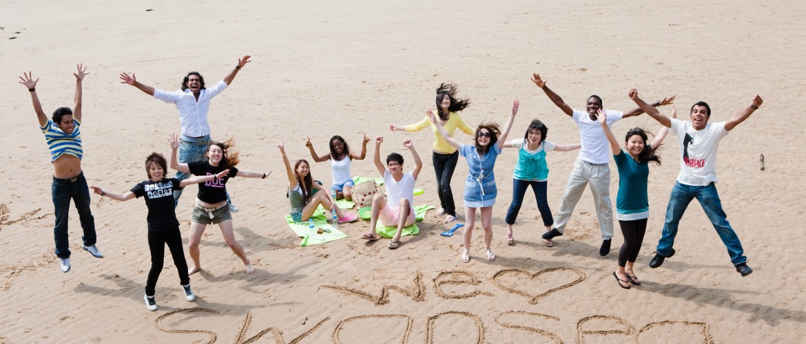Students on the beach with I love Swansea written in the sand