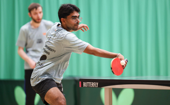 A man with a table tennis racket hitting the ball on a table tennis table