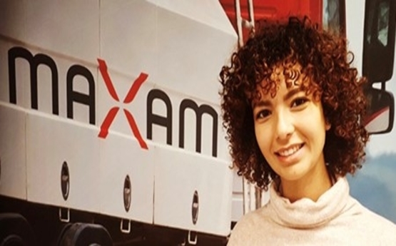 Photo of Reem standing by her new employer's, Maxam, logo.