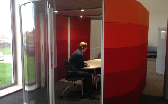 Image shows a student in dark clothing sitting inside the orange, glass fronted Bay Library Group Study Pod.