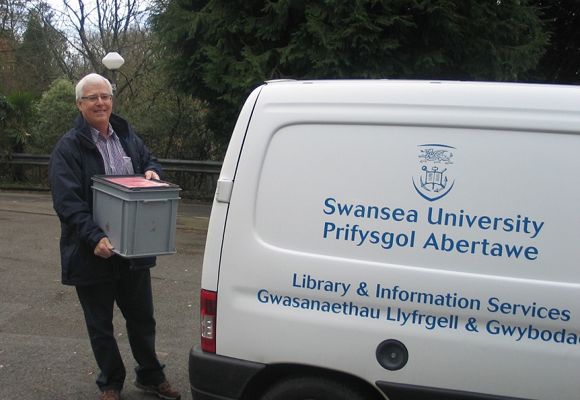 A man carrying a box of documents to a Swansea University van for delivery