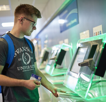 A student using their student ID card to borrow a book at the library self-issue kiosk