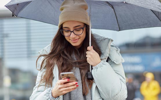 Girl holding an umbrella and looking at her phone.