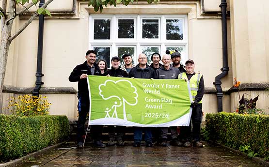 Swansea University's grounds team standing in front of Singleton Abbey holding the Green Flag 