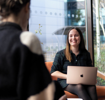 An image of a student with a laptop talking to another student.