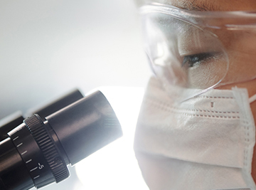 masked scientist looking through microscope