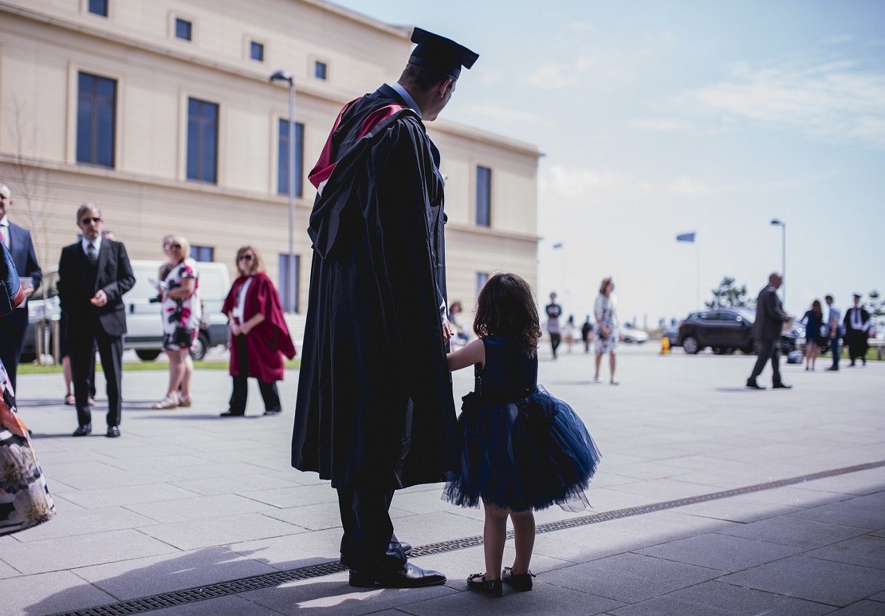 Person in graduation gown, holding hands with young girl.