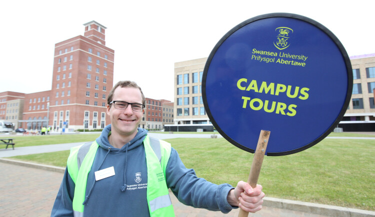 Open day volunteer holding up a campus tours sign