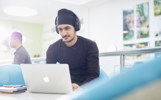 Male student wearing headphones working on a laptop