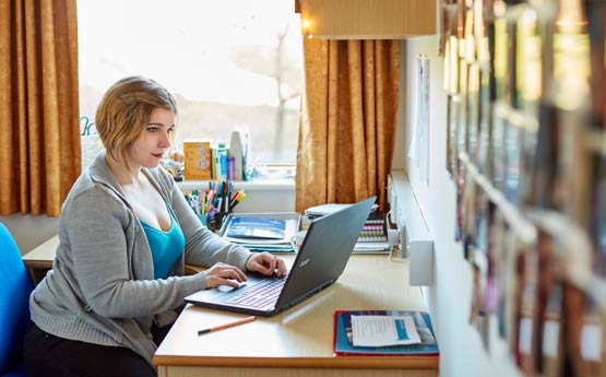 A student sat at her laptop at a desk in student residence