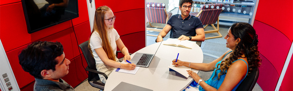 2 men and 2 women sitting round a table with laptops, papers and pens having a discussion