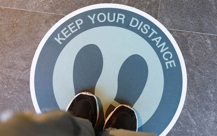 A man's feet standing on a floor sign that says 'Keep your distance' 