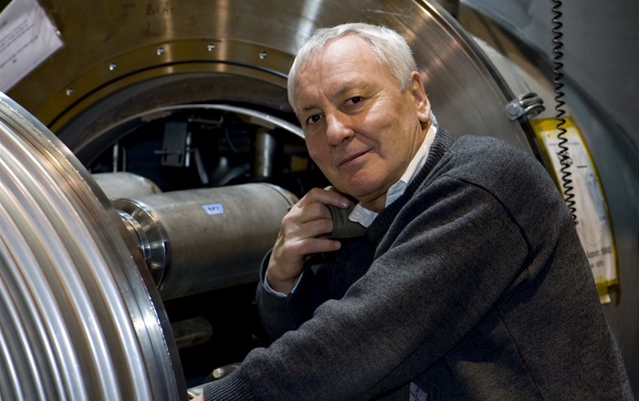 A photo of Professor Lyn Evans standing next to the Large Hadron Collider.
