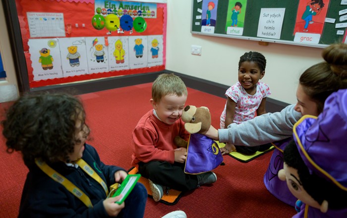 Laughing children play with Doti and Dewin cuddly toys at a Mudiad Meithrin playgroup. 