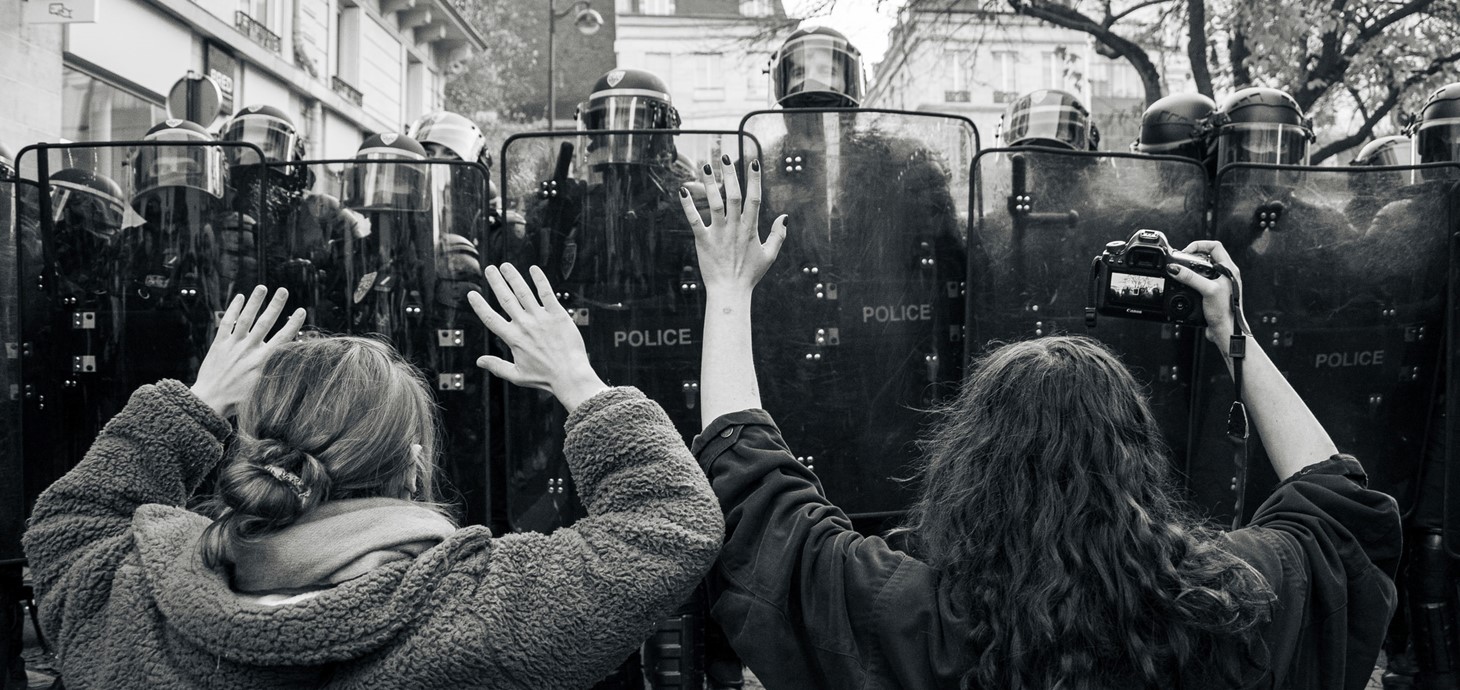 Two protestors - one with a camera - in front of a police line at a Paris demonstration against a new security law, December 2020. Credit: Koshu Kunii on Unsplash