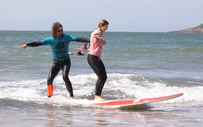 Man and woman in wetsuits standing up on a surfboard in the sea