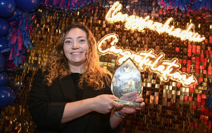 Katie Harris holds her award in front of a light up sign that says ‘Congratulations’.