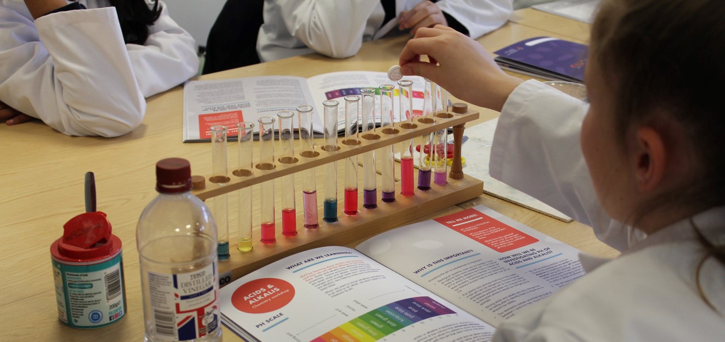 A student doing an acid and alkali experiment using a pipette and test tubes with different colour liquids.