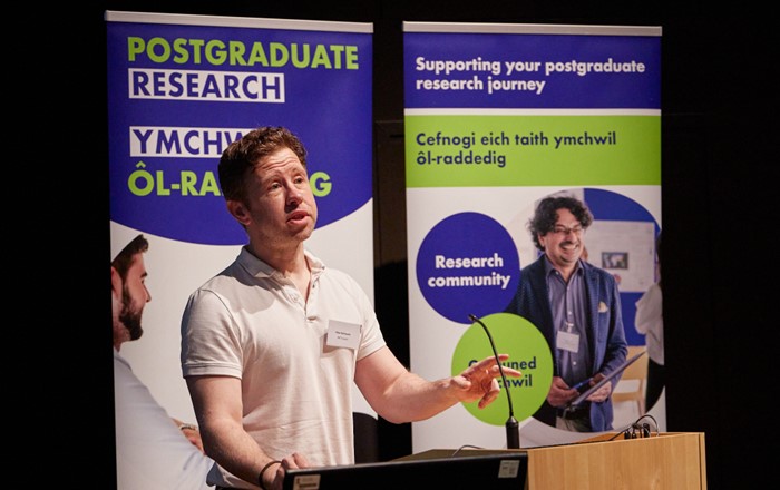 Eilian Richmond stood at a lectern, delivering his three minute thesis