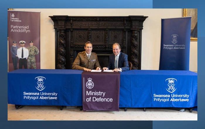 The Commanding Officer of the Wales Universities Officers’ Training Corps, Lieutenant Colonel Andrew Child pictured sitting in front of a large fireplace signing the Armed Forces Covenant with Professor Paul Boyle, Vice-Chancellor of Swansea University. 