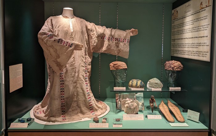 Historical tunic on a mannequin in an exhibition alongside smaller artifacts.